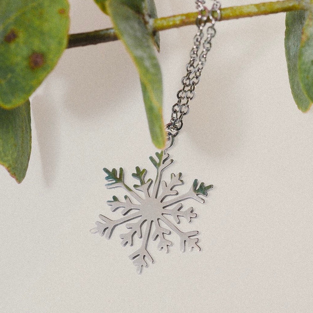 
“Collar en forma de copo de nieve de acero inoxidable, colgado de una rama, con un diseño inspirado en la ciudad de Burgos.”